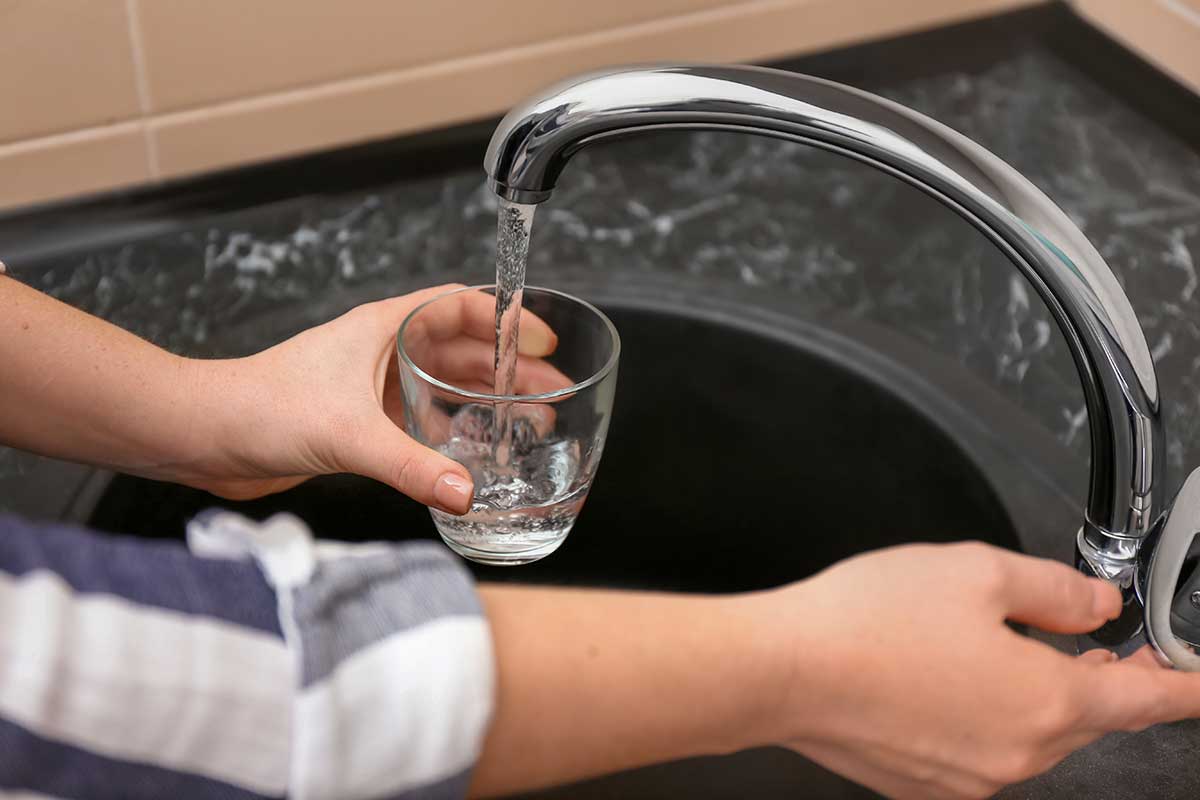 mulher enchendo copo com agua na torneira da pia de cozinha